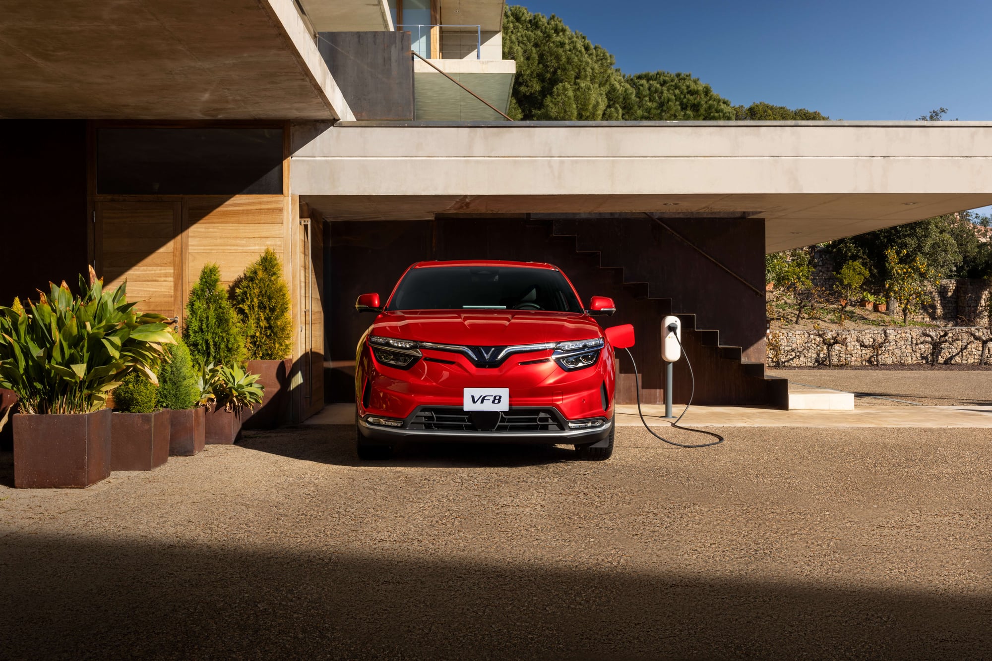 VinFast VF 8 in red plugged into a home charger under an architectural canopy